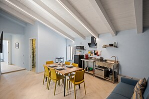Cocina moderna con microondas, estufa y lavaplatos, un comedor con sillas amarillas y un sofá azul.