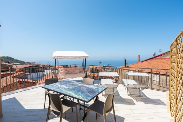 An outdoor terrace with a table and chairs, a white umbrella, and a view of the sea. - Apartment 'Deluxe Zenone' with Sea View, Wi-Fi and Air Conditioning (Ascea)
