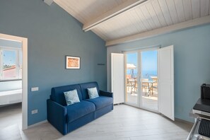 A room with a blue sofa, a framed picture on the wall, and a sliding glass door leading to an outdoor area with a table and chairs. - Apartment 'Deluxe Zenone' with Sea View, Wi-Fi and Air Conditioning (Ascea)