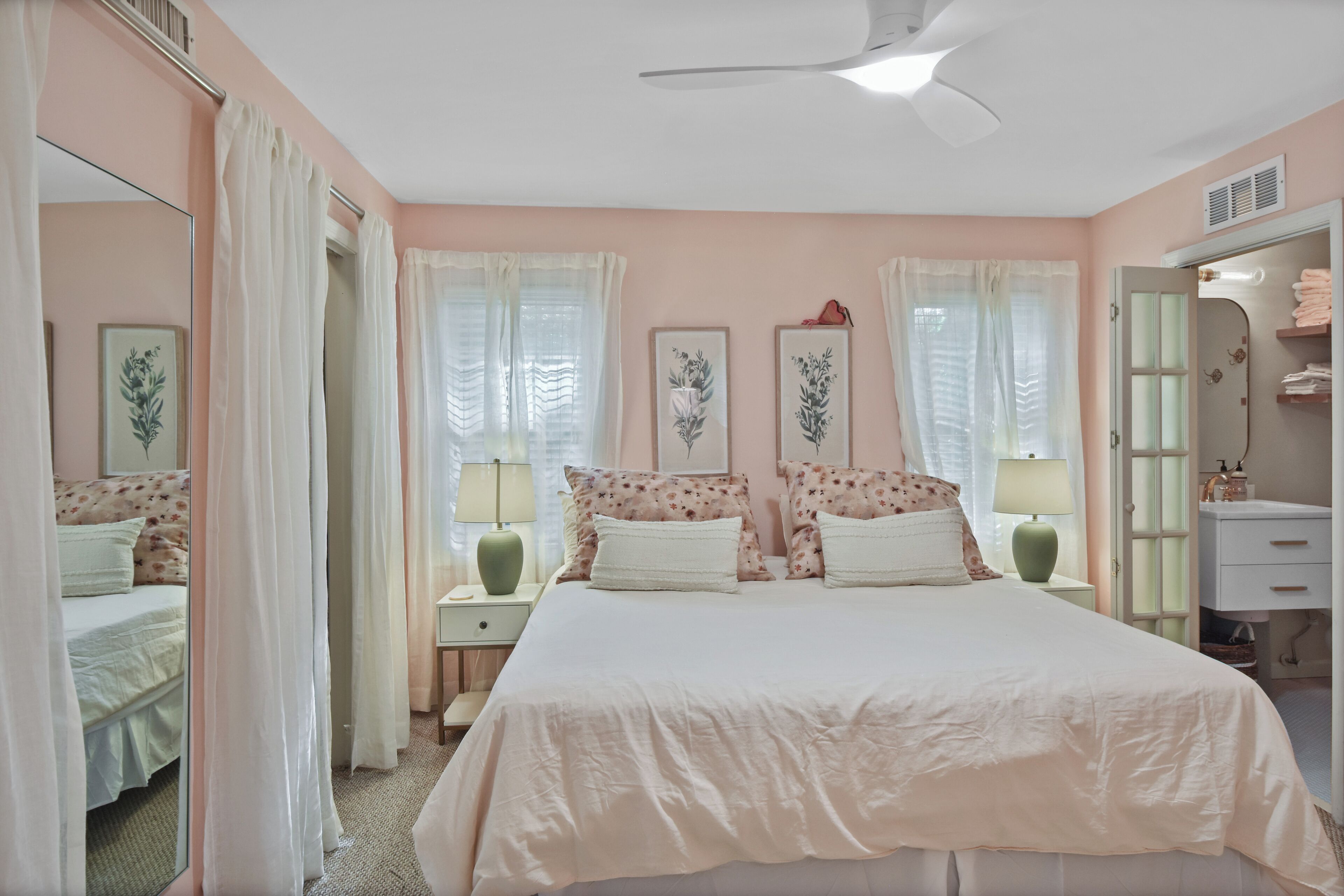 A bedroom with a large bed, two bedside tables, a nightstand, a mirror, and a wardrobe.