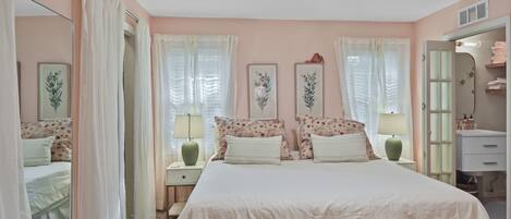 A bedroom with a large bed, two bedside tables, a nightstand, a mirror, and a wardrobe.