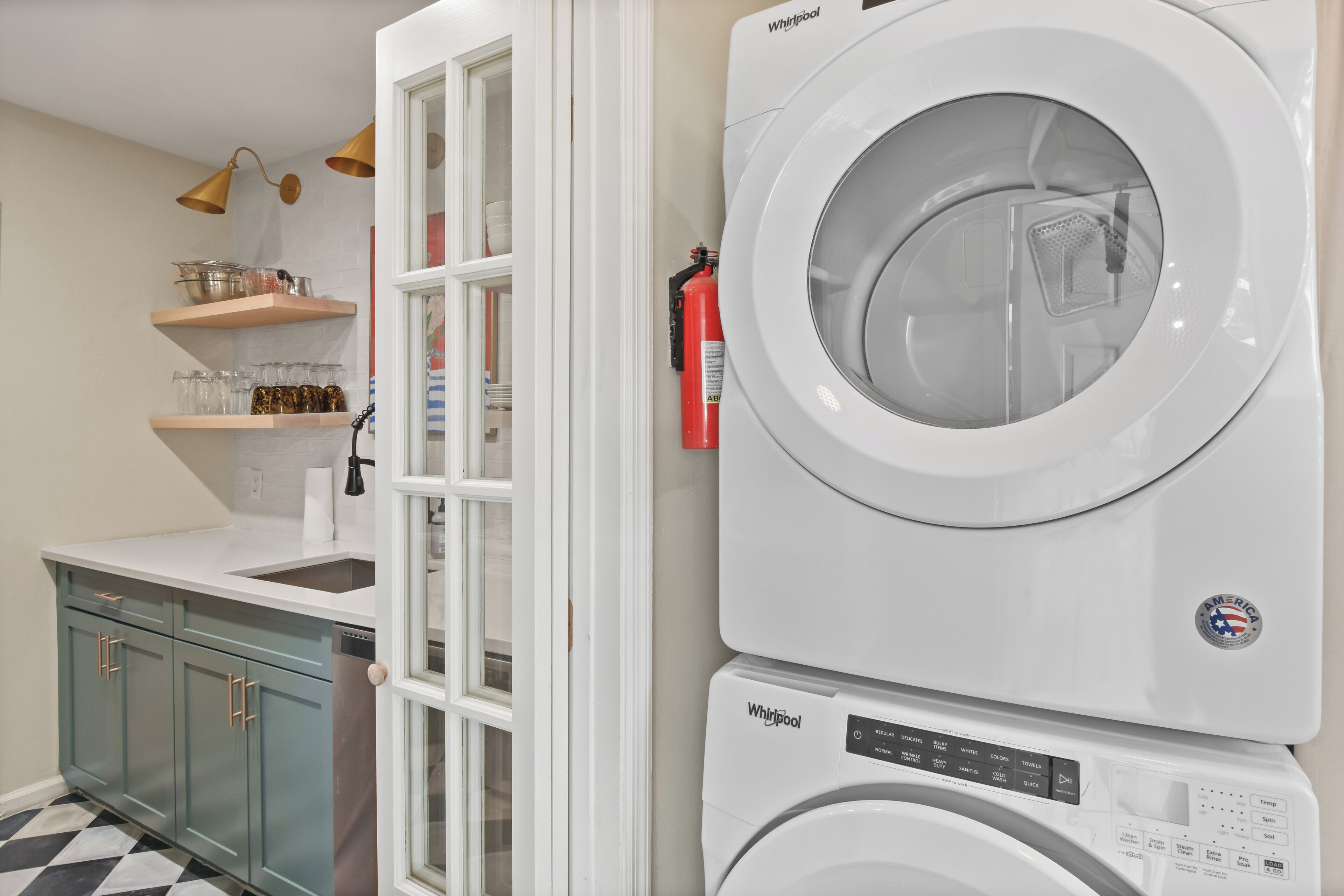 A laundry room with a stacked washer and dryer, a fire extinguisher, and a window with a view of the outside.