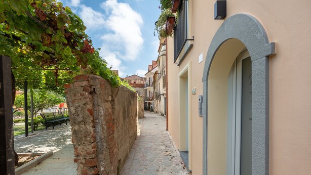 A narrow cobblestone street with a brick wall on one side and a building with a door on the other. - Apartment 'Senofane' with Wi-Fi and Air Conditioning (Ascea)