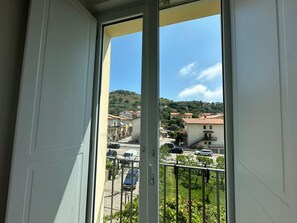 A balcony with a view of a residential area, including houses and a hilly landscape.