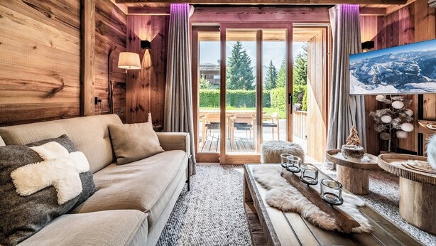 Interior acogedor de una cabaña de madera con sofá, televisor y comedor con mesas y sillas de madera.