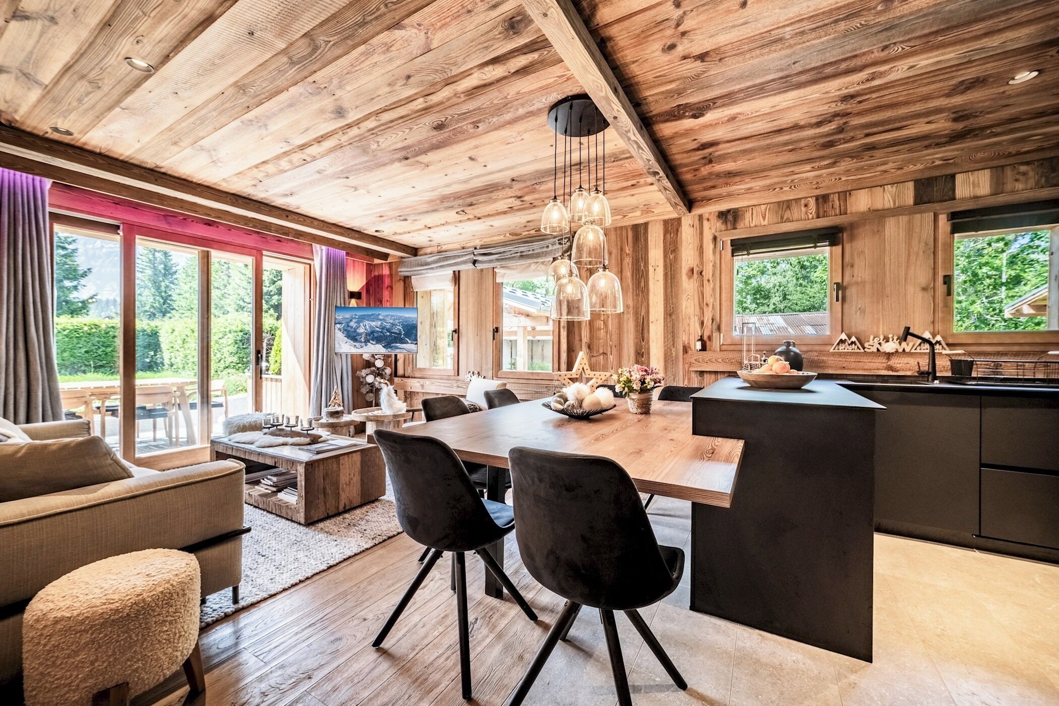 Une cuisine moderne avec un plafond en bois, un coin repas doté d’une grande table et de chaises, et une vue sur l’extérieur.