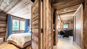 Interior de una cabaña de madera con una cama, un escritorio y vistas al exterior.