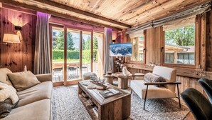 Una sala de estar acogedora con techo de madera, un ventanal con vistas a la vegetación, un televisor de pantalla plana y una chimenea.