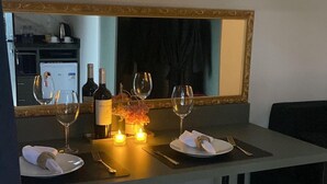 A dining area with a table set for two, a mirror above the table, and a kitchenette in the background. - Hotel Villa Verde by Easy Hotéis (Sao Bento do Sul)