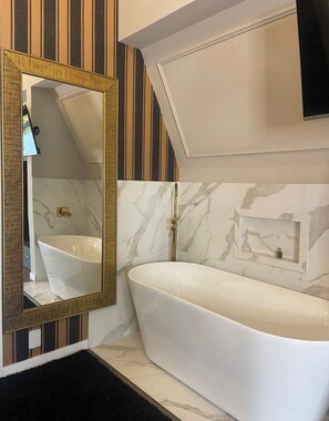 A modern bathroom with a freestanding bathtub, a large mirror with a gold frame, and marble-patterned walls. - Hotel Villa Verde by Easy Hotéis (Sao Bento do Sul)
