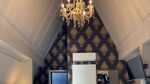 A bedroom with a large bed, a chandelier, a bathroom with a bathtub, and a patterned wall. - Hotel Villa Verde by Easy Hotéis (Sao Bento do Sul)