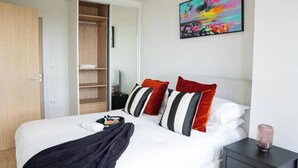 Habitación de hotel con cama, mesita de noche, armario y un cuadro abstracto y colorido en la pared.