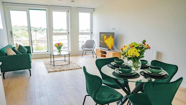 Una sala de estar moderna con comedor, ventanas amplias, televisor de pantalla plana y vistas al exterior.