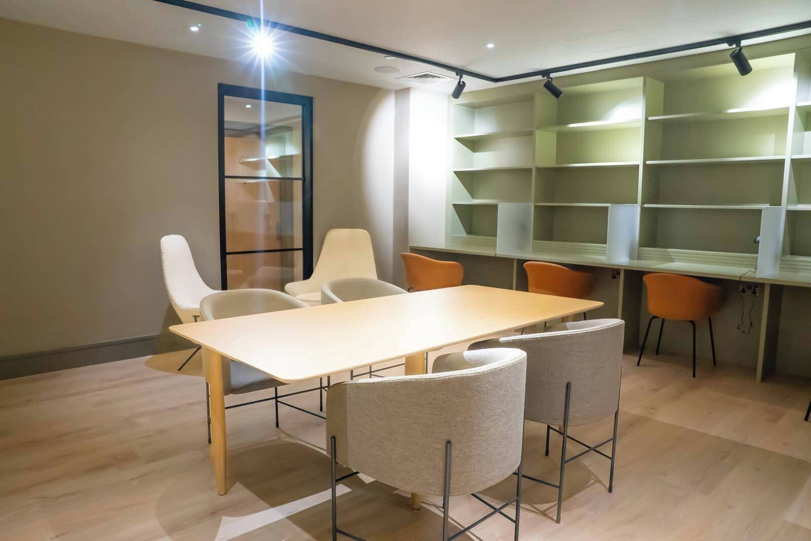 A conference room with a long table, four chairs, and a bookshelf with multiple shelves.