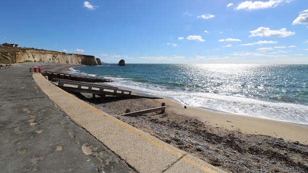 Une route côtière bordée d’une plage, de falaises et surplombant un ciel dégagé.