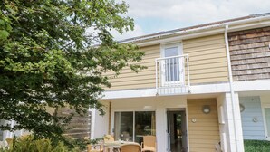 Une maison à deux étages dotée d’un patio aménagé avec des meubles en osier et une petite table.