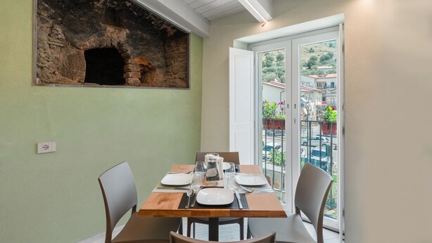 A dining area with a stone fireplace, a balcony with a view of the city, and a table set for two. - Apartment 'Deluxe Melisso' with Wi-Fi and Air Conditioning (Ascea)
