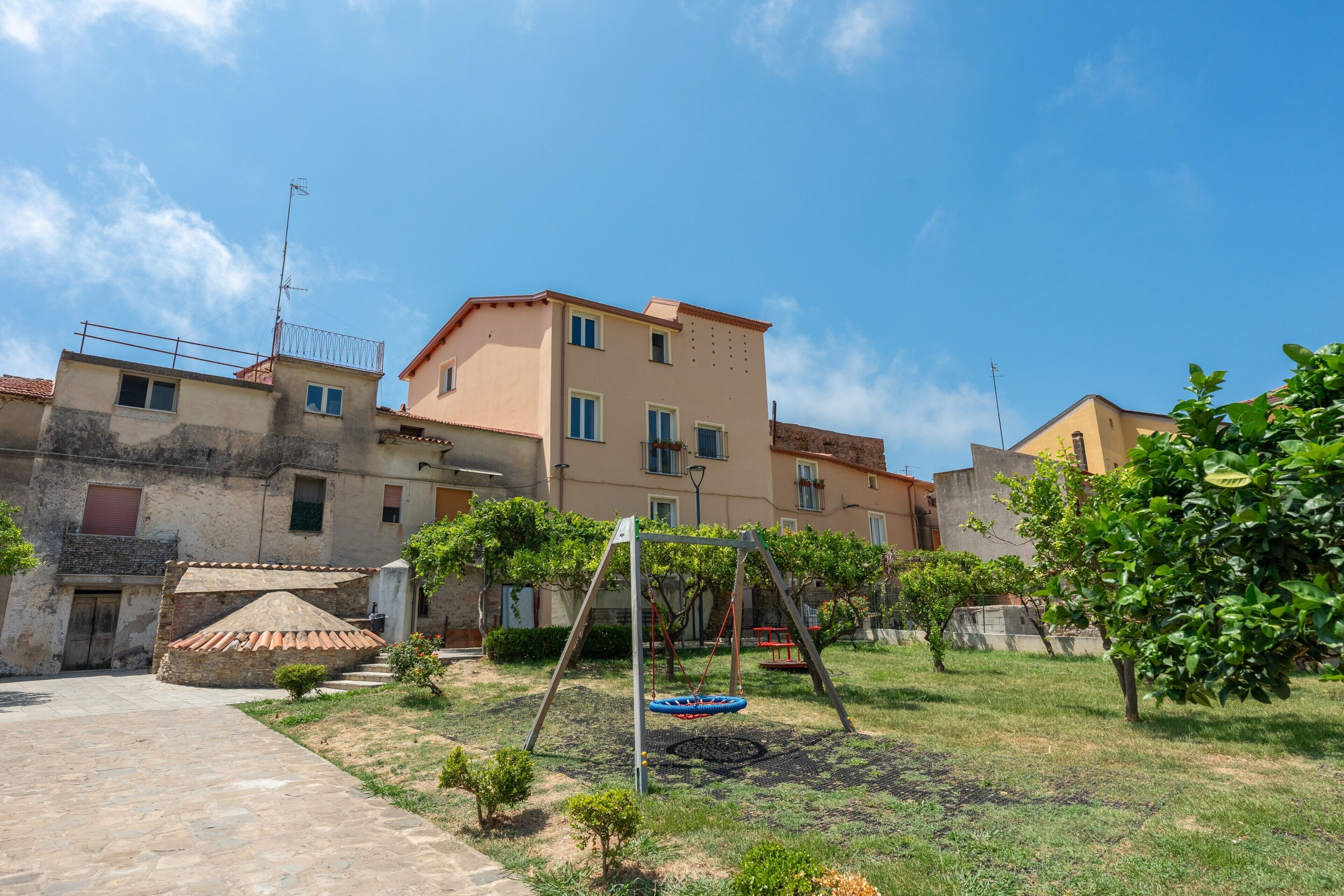 A courtyard with a swing set, a small garden, and buildings in the background.