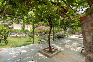 Un espace extérieur aménagé avec un revêtement pavé, des bancs, un arbre et un terrain herbeux.