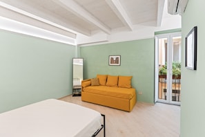 Ein Zimmer mit einem Bett, einem Sofa, einem Fenster und einer Tür zu einem Außenbereich.