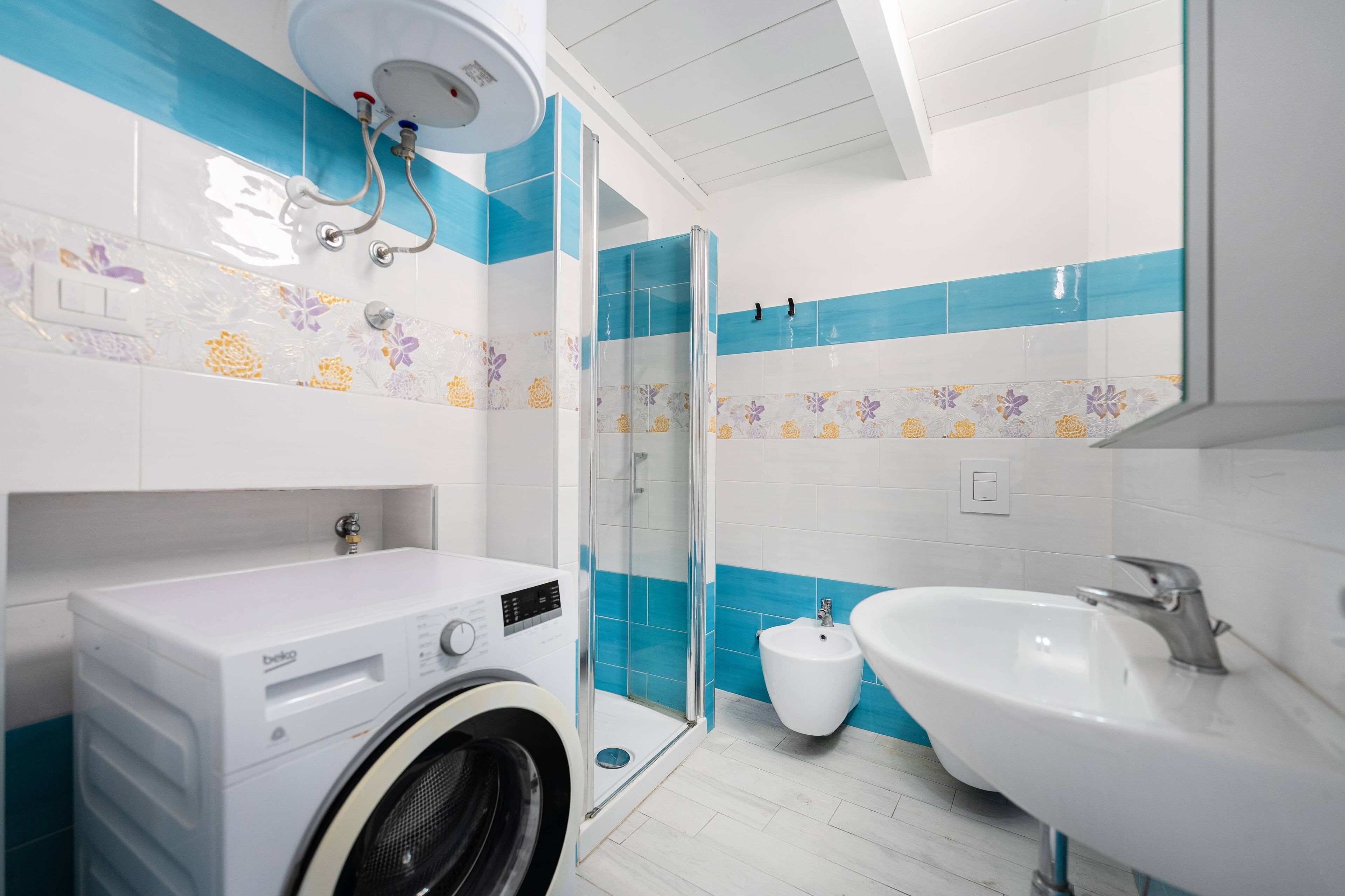 A modern bathroom with a washing machine, a glass-enclosed shower, and a sink.