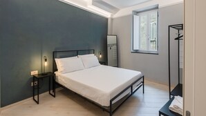Une chambre à coucher comprenant un lit, des tables de chevet, une commode, une fenêtre et un miroir fixé au mur.