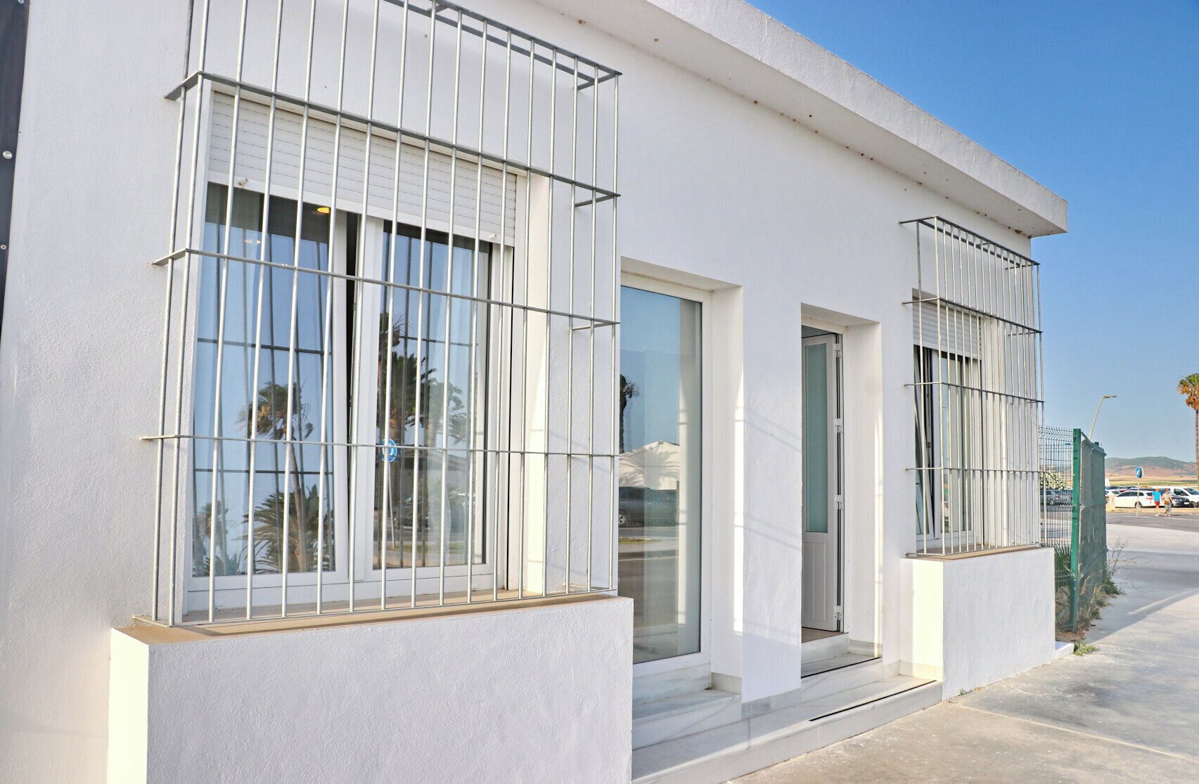 A modern building with large windows and metal bars, featuring a clean, white exterior and a clear sky.