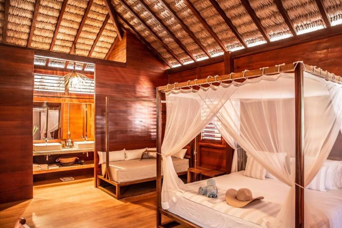 A wooden room with a four-poster bed, a vanity with a mirror, and a ceiling with a thatched roof.