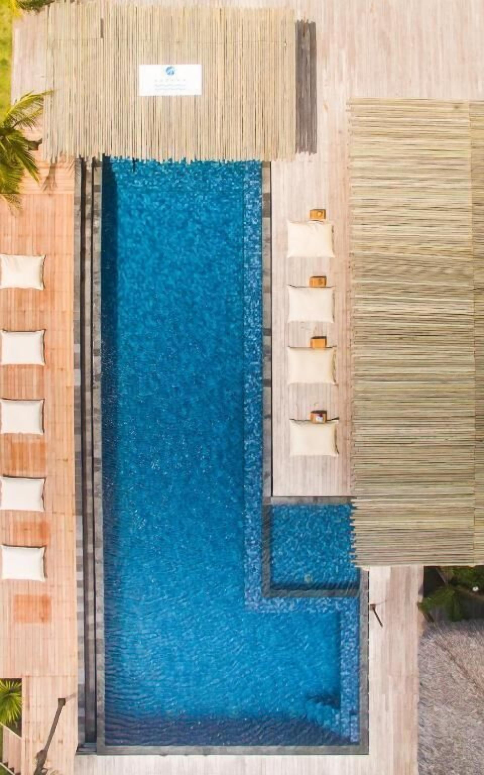 A rectangular swimming pool with clear blue water, surrounded by wooden deck areas with lounge chairs.