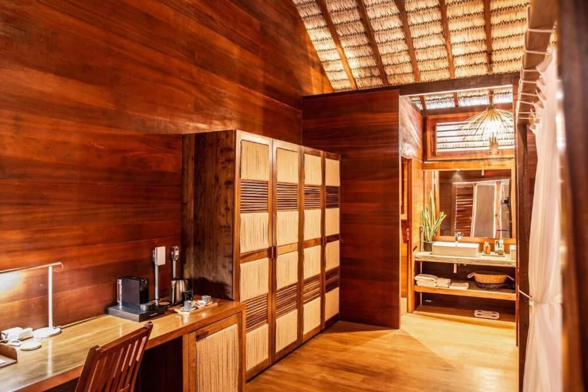 A wooden room with a desk, a cabinet, and a bathroom with a mirror and sink.