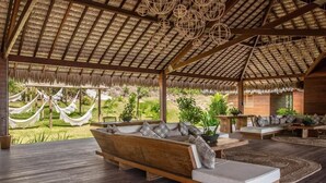 A spacious outdoor lounge area with wooden furniture, a thatched roof, and hanging wicker lamps. - Kabana Hotel (Cruz)