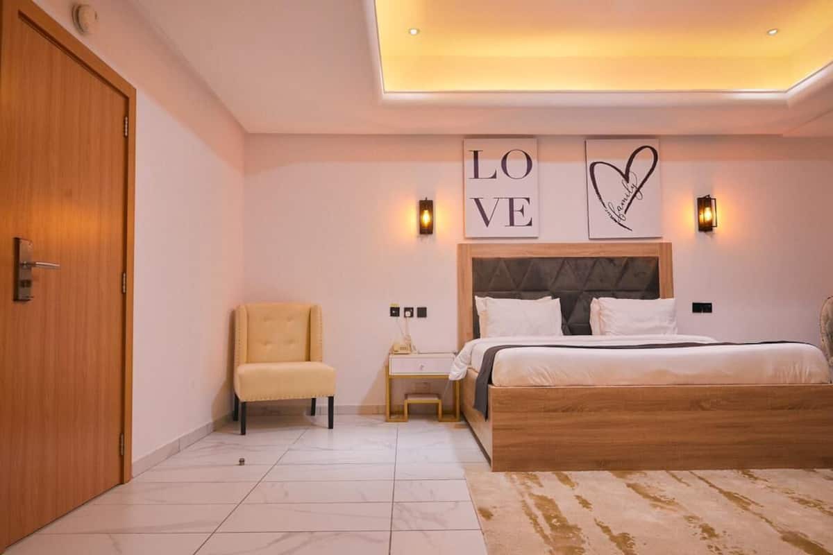 Un dormitorio con cama, una silla, una mesita de noche y una obra de arte en la pared.