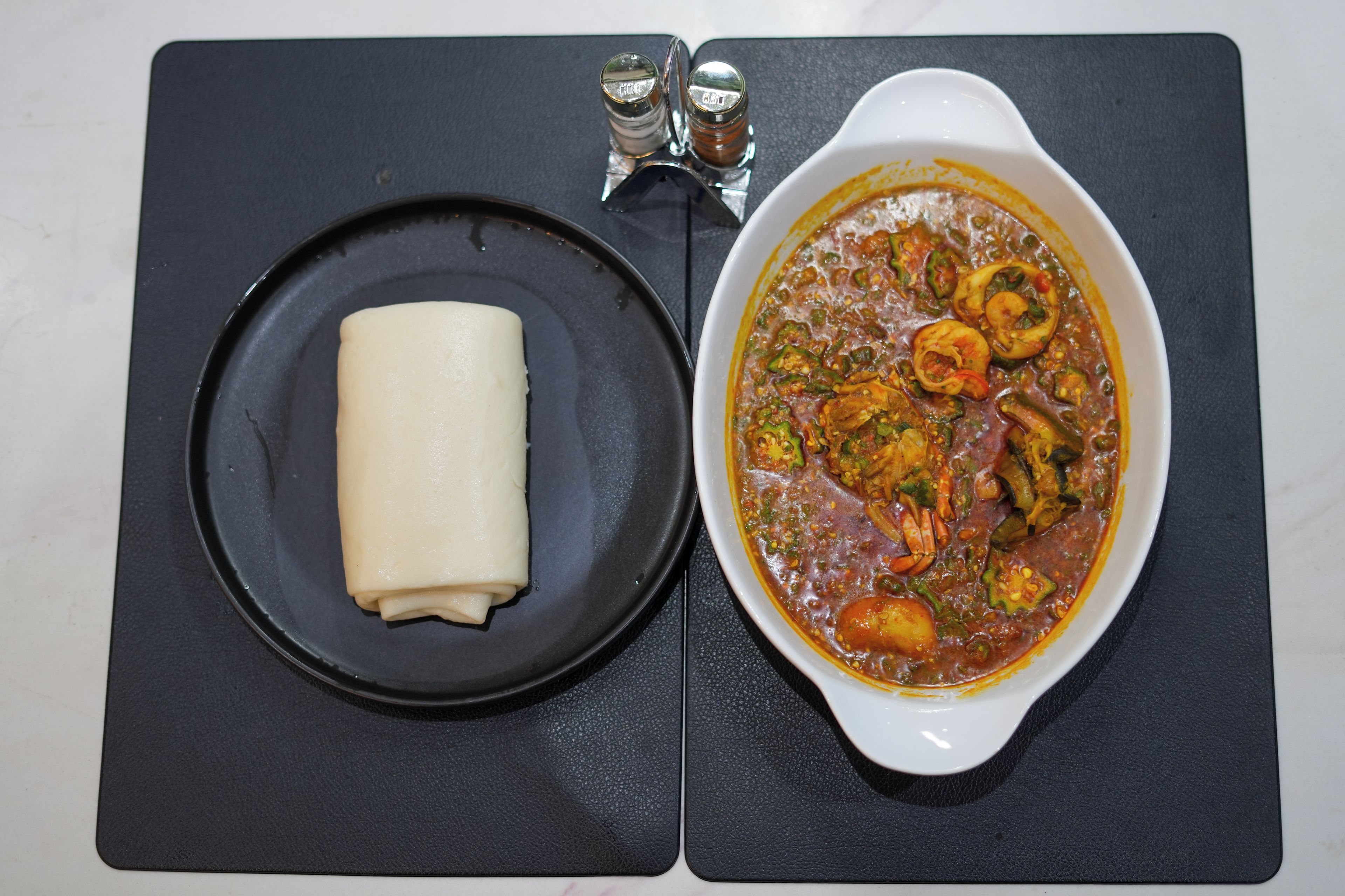 A black plate with a white item and a white bowl with a stew.