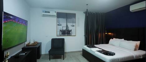 Ein Hotelzimmer mit Bett, Schreibtisch mit Fernseher, Klimaanlage, Stuhl und einem Bild an der Wand.