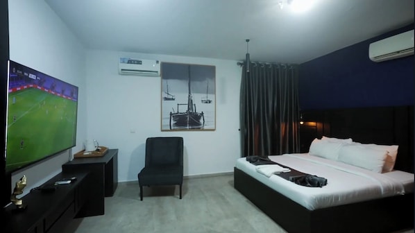 Une chambre d’hôtel avec un lit, un bureau avec une télévision, un climatiseur, une chaise et un tableau au mur.