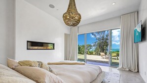 Une chambre spacieuse avec un grand lit, un téléviseur fixé au mur et une vue sur la plage grâce à de grandes fenêtres du sol au plafond.