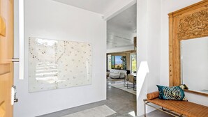 Un intérieur moderne agrémenté d’une grande œuvre d’art abstraite, d’un miroir à cadre en bois et d’un banc avec un coussin à motifs.