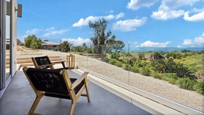 Un balcon avec deux chaises en bois et une table, donnant sur un paysage pittoresque avec des arbres et une vue sur la mer.