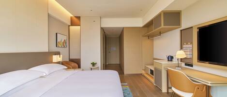 Una habitación de hotel moderna con una cama grande, un escritorio, una silla, un televisor y una pequeña mesa con lámpara.