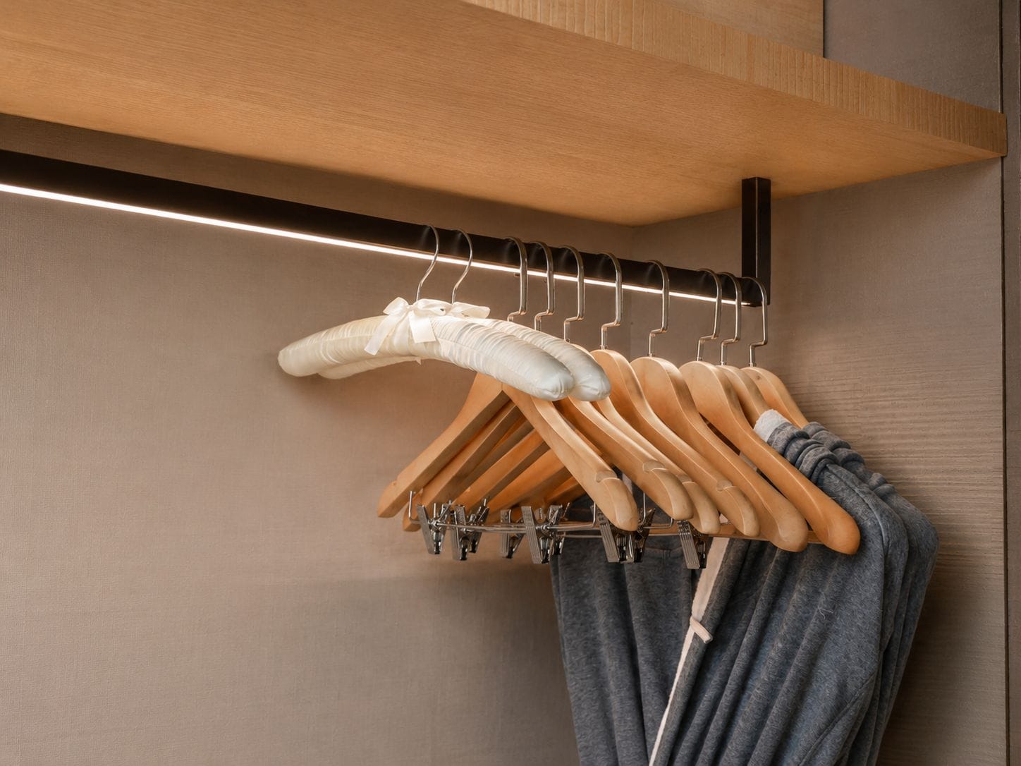 Een houten kapstok met meerdere ophanghaakjes, waaronder een paar witte balletveters en een grijze kledingstuk.