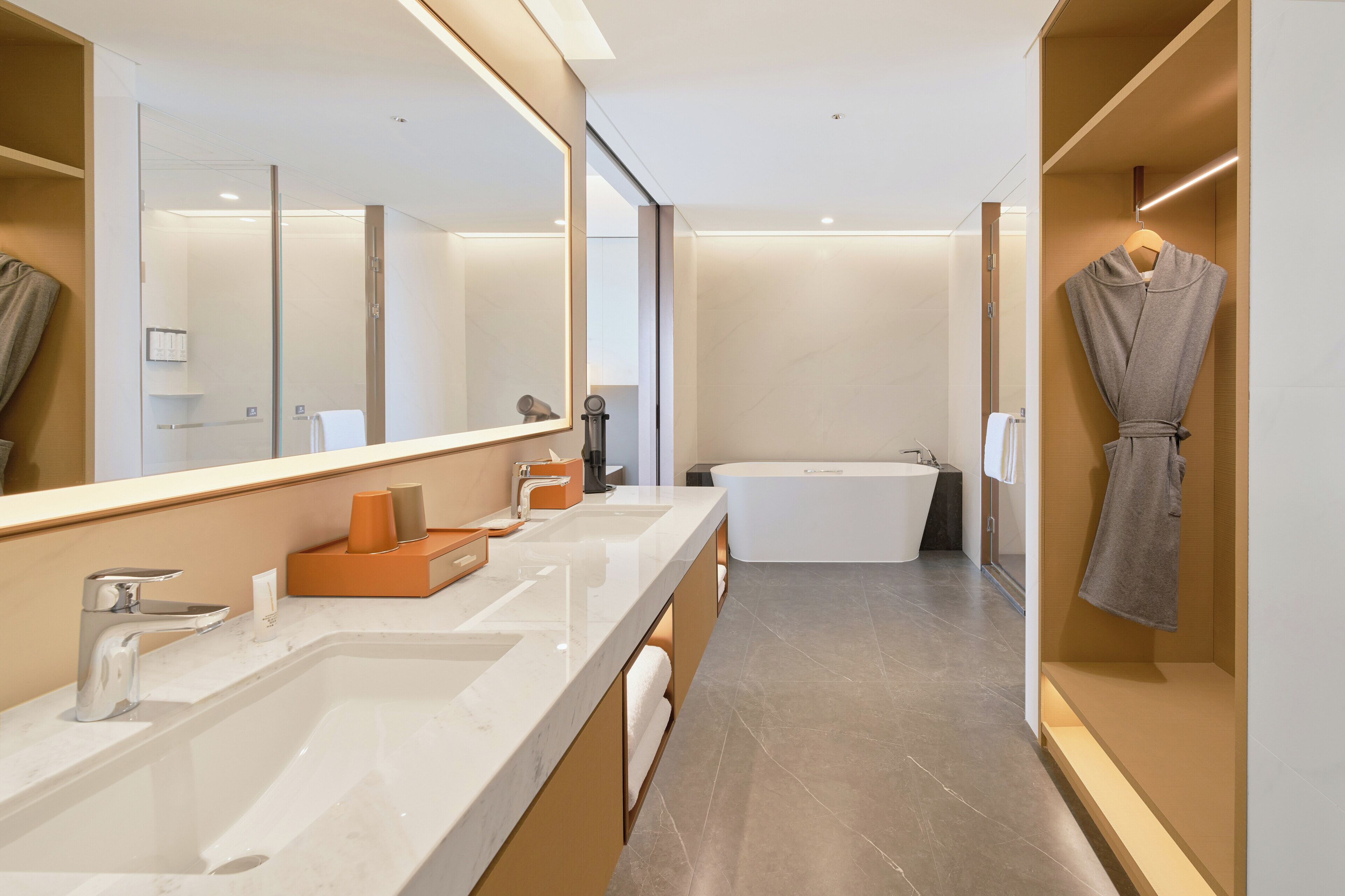 Un baño moderno con un espejo grande, dos lavamanos, una bañera y una bata colgada en un perchero.