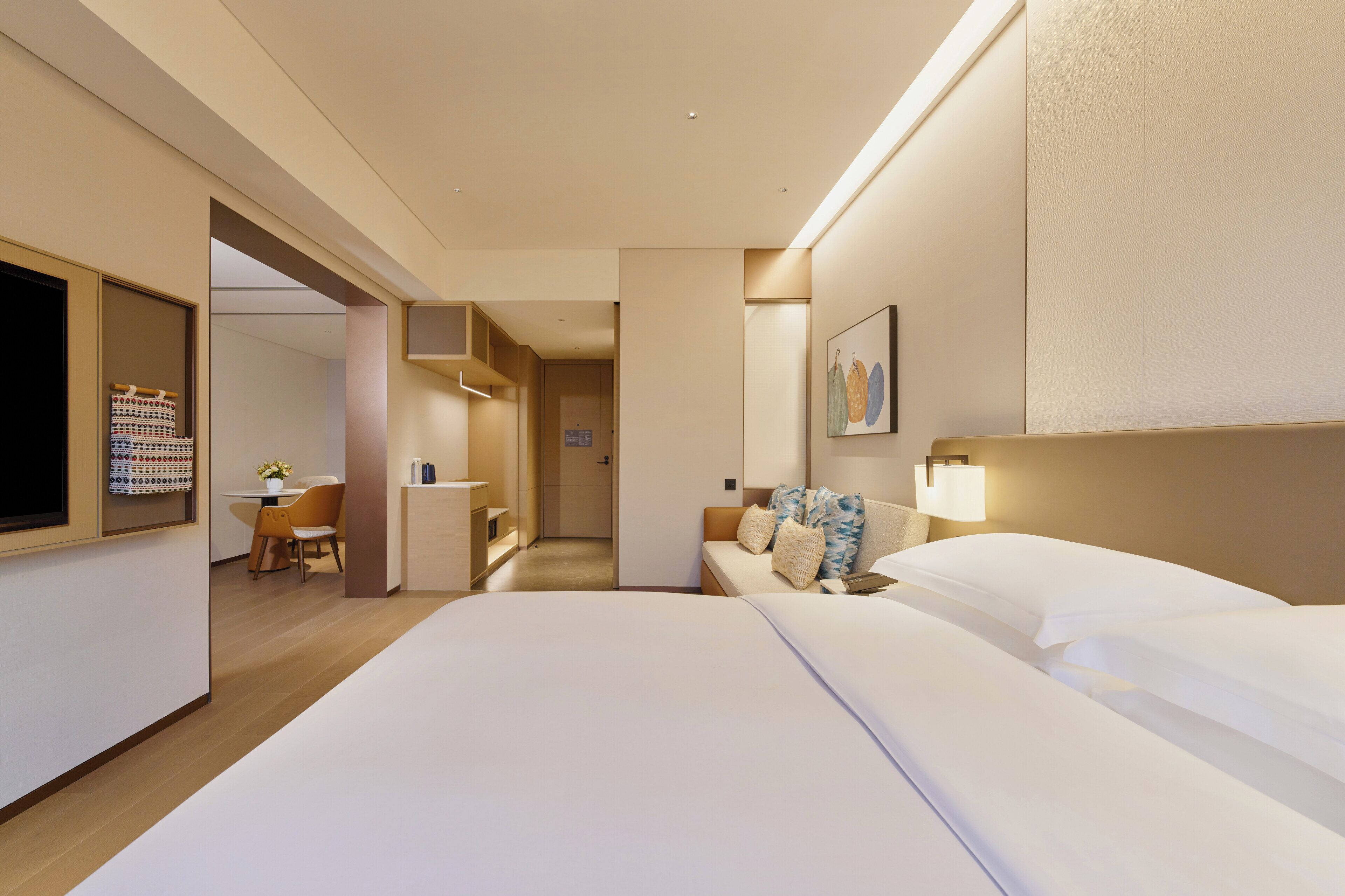 Quarto de hotel com cama, mesa de cabeceira, luminária e um pequeno espaço de estar com cadeira e mesa.