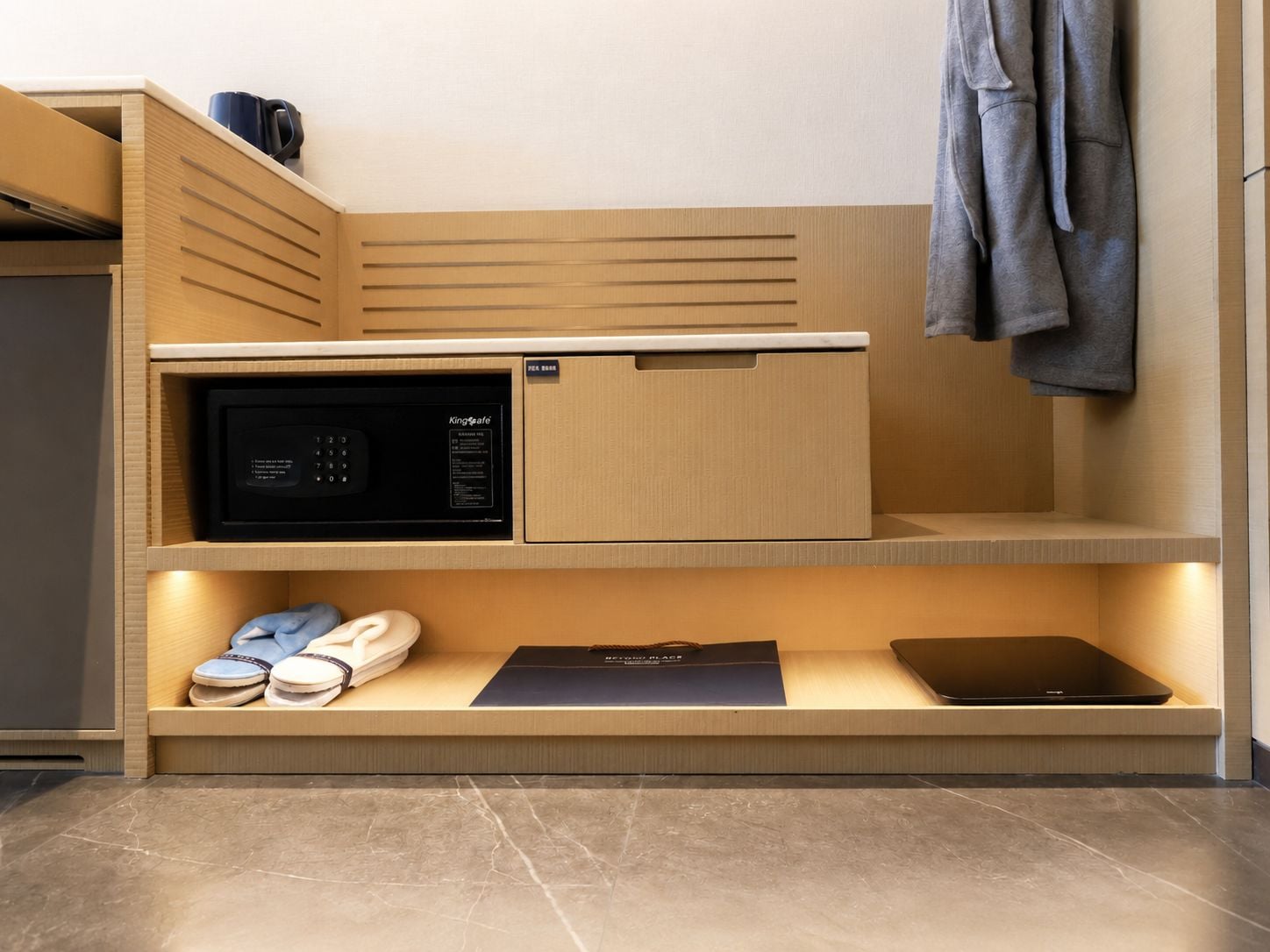 A compact kitchenette with a microwave, a small fridge, and a shelf with shoes and a laptop.