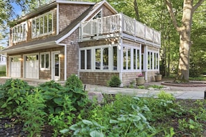 A two-story house with a balcony, large windows, and a garden with various plants.