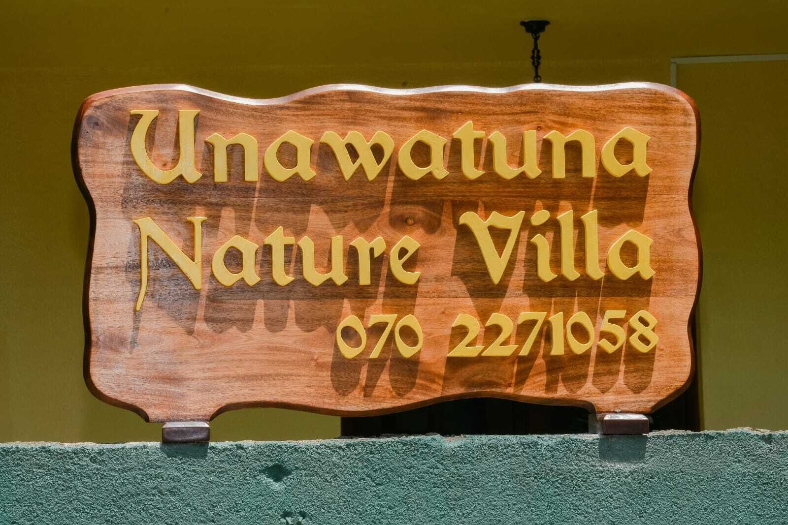 Et træskilt med teksten "Unawamata Nature Villa" og telefonnummeret "070 2271058".