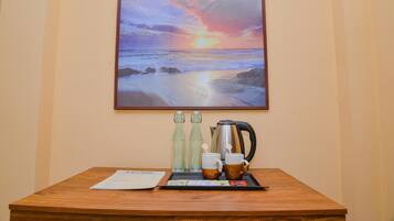 Una mesa de madera con una bandeja que contiene una cafetera, dos tazas y dos botellas, frente a una pared con un cuadro de un atardecer enmarcado.