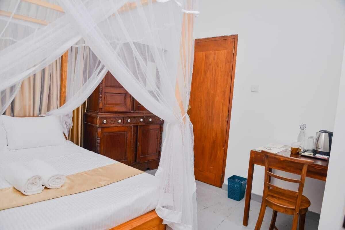 Un dormitorio con cama con dosel, un aparador de madera, un escritorio con silla y un cubo de basura azul.