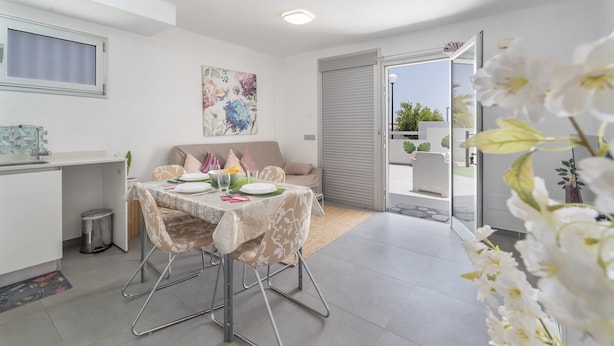 Un comedor moderno con una mesa preparada para cuatro personas, un sofá, una ventana y una puerta que da al exterior.