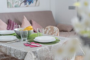 Une table à manger dressée avec des assiettes, des verres et des couverts, avec un canapé et des coussins en arrière-plan.