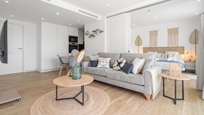 A modern living room with a grey sofa, a round coffee table, and a dining area with a wooden table and chairs. - AL4-2023 ESTEPONA - APARTMENT - ALCAZABA LAGOON (Casares)